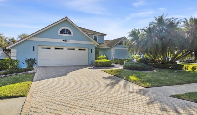 view of front of home featuring stucco siding, decorative driveway, a front lawn, and an attached garage