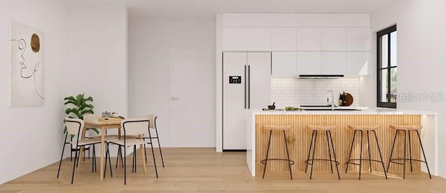 kitchen featuring a breakfast bar, white cabinetry, decorative backsplash, kitchen peninsula, and light wood-type flooring