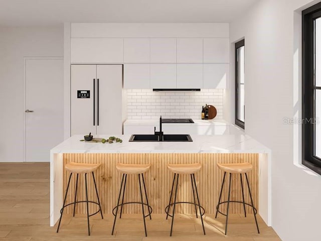 kitchen with paneled refrigerator, backsplash, a kitchen breakfast bar, and white cabinets