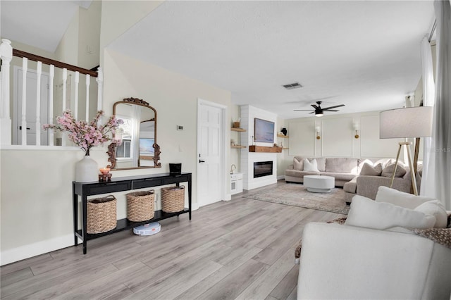 living room featuring light hardwood / wood-style floors, a large fireplace, and ceiling fan