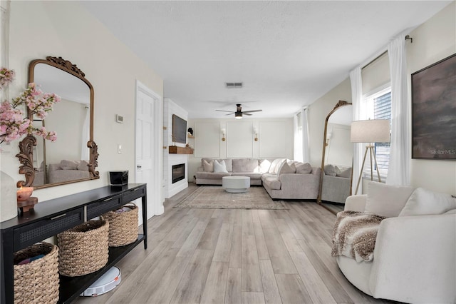 living area featuring light wood finished floors, visible vents, a ceiling fan, and a glass covered fireplace