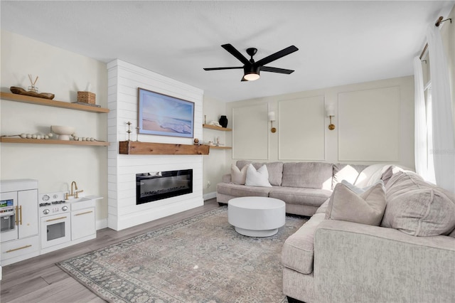 living room with a ceiling fan, wood finished floors, and a large fireplace