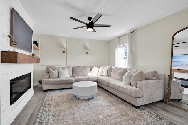 living room with a glass covered fireplace, wood finished floors, and a ceiling fan