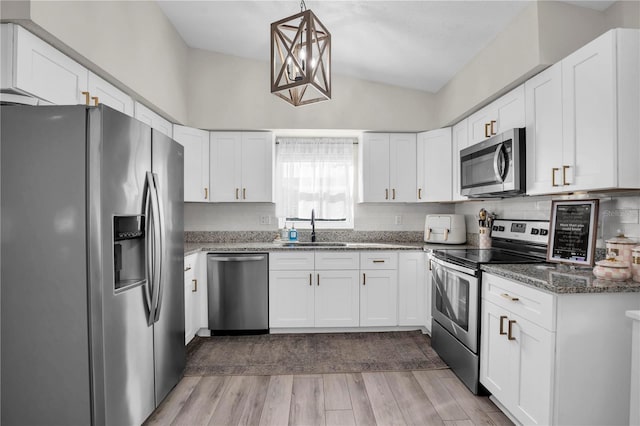 kitchen with a sink, dark stone countertops, stainless steel appliances, white cabinets, and light wood finished floors