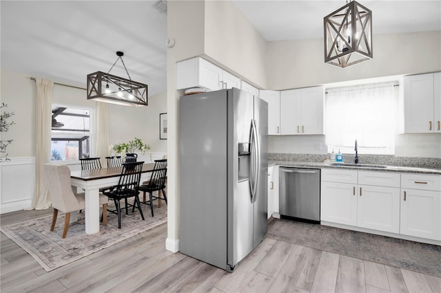 kitchen featuring light wood-style flooring, a sink, white cabinetry, stainless steel appliances, and light stone countertops