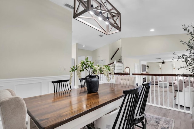 dining area with stairway, wood finished floors, a wainscoted wall, visible vents, and a decorative wall