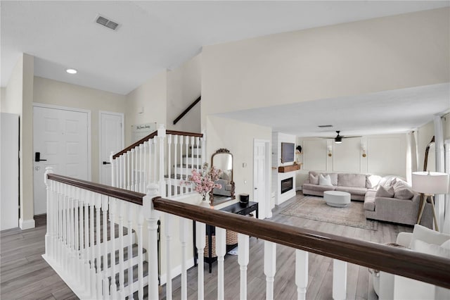 stairway featuring visible vents, wood finished floors, a large fireplace, baseboards, and ceiling fan