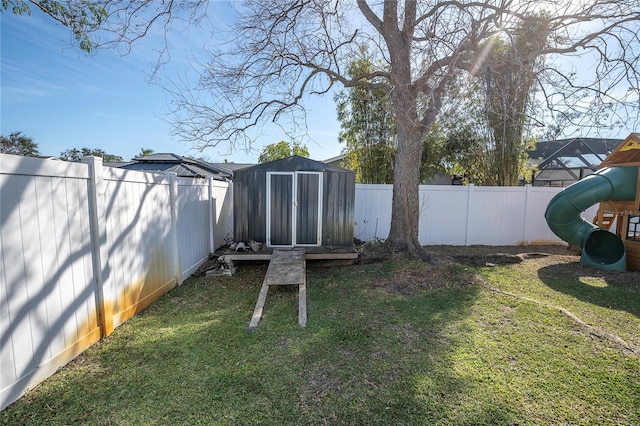 view of yard with a storage unit, an outdoor structure, a playground, and a fenced backyard