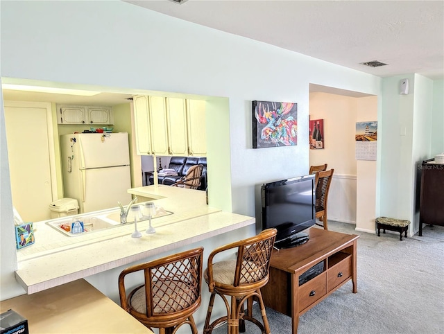 kitchen featuring sink, a kitchen breakfast bar, white refrigerator, light carpet, and cream cabinetry