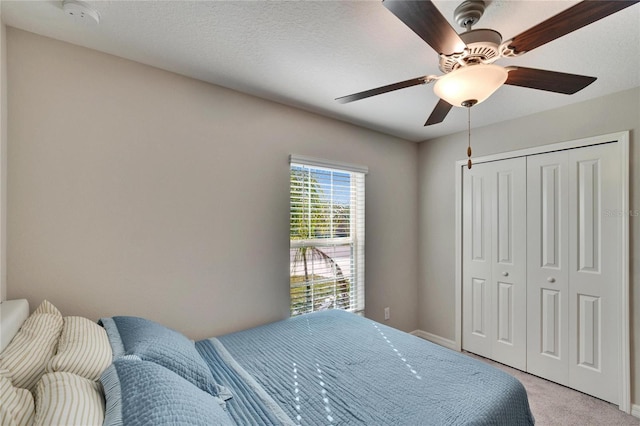 bedroom featuring a textured ceiling, ceiling fan, a closet, and light colored carpet