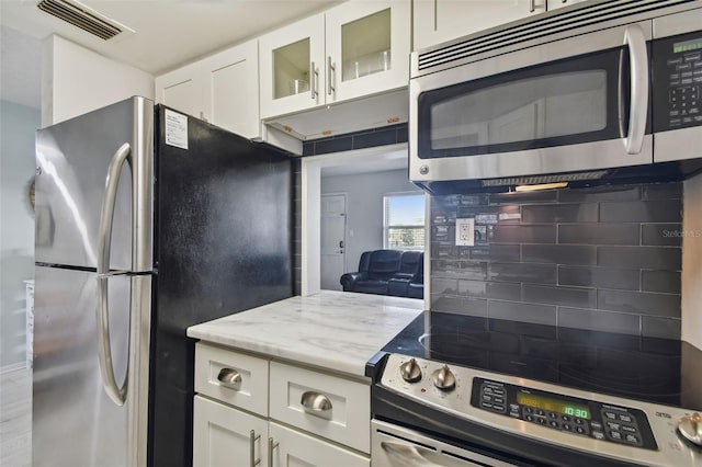 kitchen featuring white cabinetry, appliances with stainless steel finishes, backsplash, and light stone counters