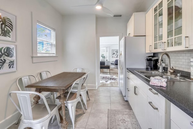 kitchen with light tile patterned flooring, sink, white cabinetry, dark stone counters, and decorative backsplash