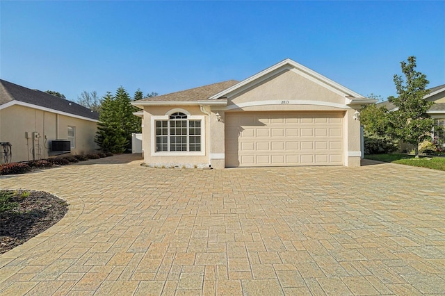 single story home with an attached garage, central AC unit, decorative driveway, and stucco siding