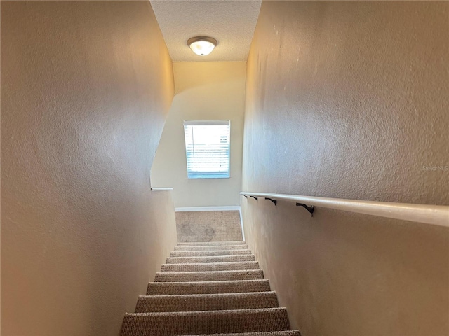 staircase with carpet floors and a textured ceiling