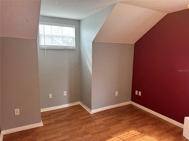 additional living space featuring hardwood / wood-style flooring, vaulted ceiling, and a textured ceiling