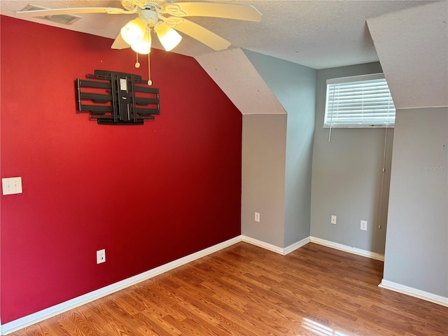 additional living space with ceiling fan, hardwood / wood-style flooring, vaulted ceiling, and a textured ceiling