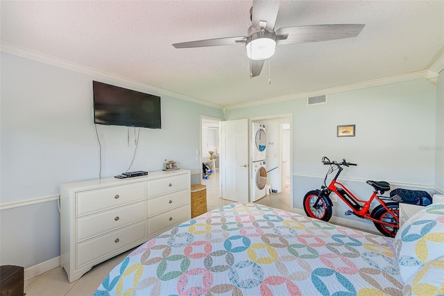 bedroom featuring light tile patterned flooring, a textured ceiling, ornamental molding, ceiling fan, and stacked washer / dryer