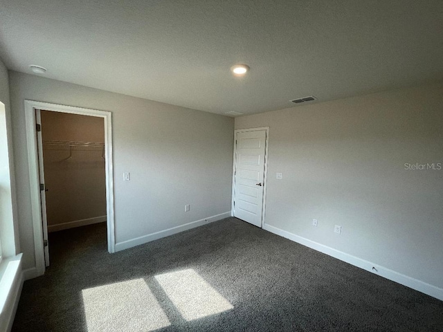 unfurnished bedroom with a walk in closet, a closet, and dark colored carpet