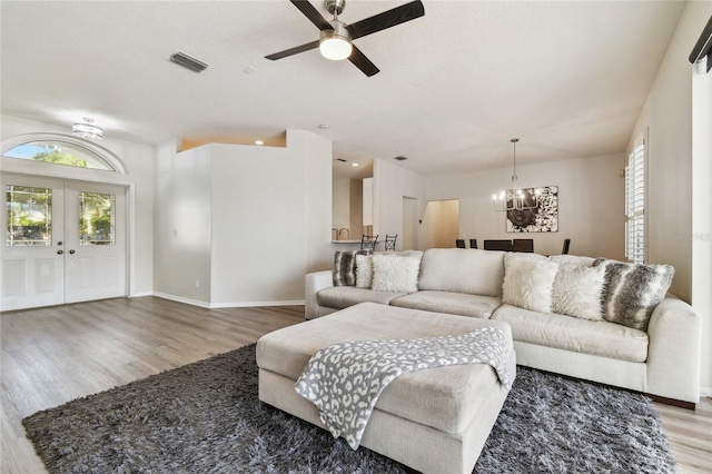 living room with hardwood / wood-style flooring, ceiling fan with notable chandelier, french doors, and a textured ceiling