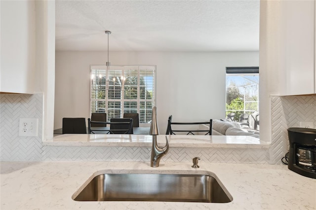 kitchen with sink, an inviting chandelier, hanging light fixtures, light stone countertops, and backsplash