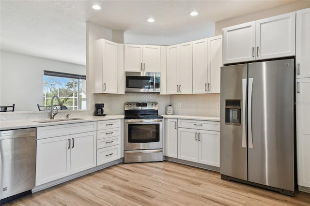 kitchen with appliances with stainless steel finishes, tasteful backsplash, sink, white cabinets, and light hardwood / wood-style flooring