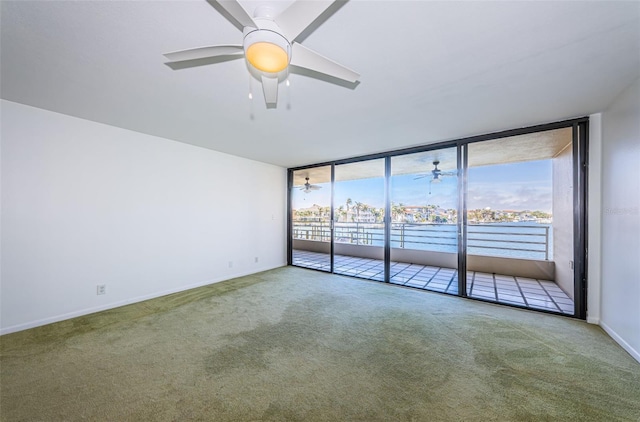 carpeted empty room featuring a ceiling fan, expansive windows, and baseboards