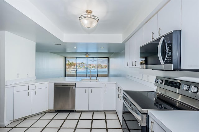 kitchen with stainless steel appliances, a raised ceiling, light countertops, white cabinetry, and a peninsula