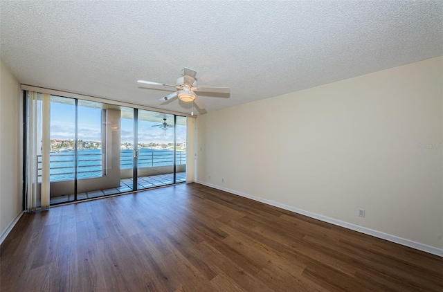 empty room with a textured ceiling, dark wood-style flooring, a ceiling fan, baseboards, and expansive windows