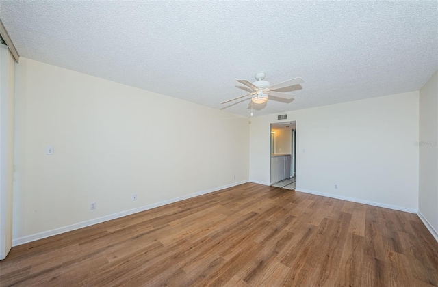 spare room with a ceiling fan, visible vents, a textured ceiling, and wood finished floors