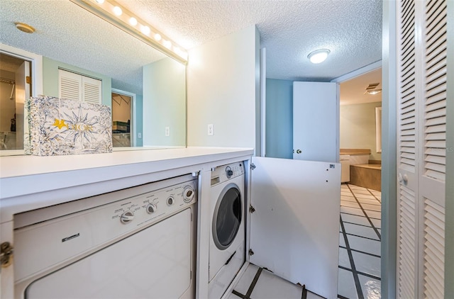 laundry room with laundry area, light tile patterned floors, washer and clothes dryer, and a textured ceiling