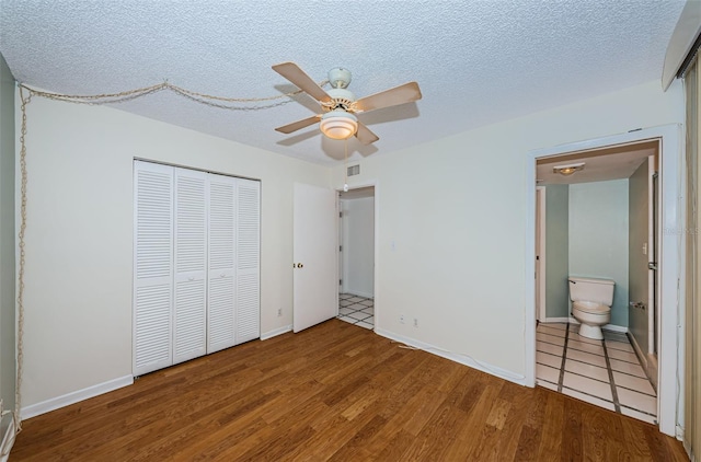 unfurnished bedroom with a closet, a ceiling fan, a textured ceiling, ensuite bath, and wood finished floors