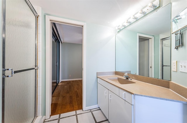 full bath with a shower with shower door, tile patterned floors, baseboards, and vanity