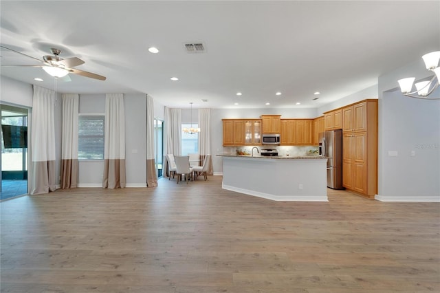 kitchen with pendant lighting, stainless steel appliances, light hardwood / wood-style flooring, and a center island with sink