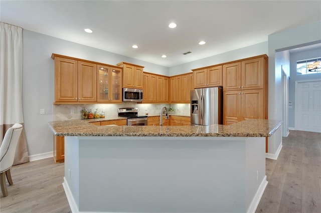 kitchen featuring light stone counters, appliances with stainless steel finishes, a center island with sink, and backsplash