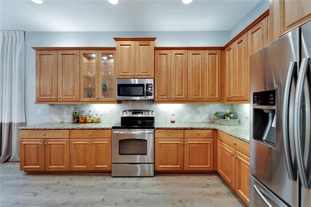 kitchen with light stone counters, decorative backsplash, stainless steel appliances, and light wood-type flooring