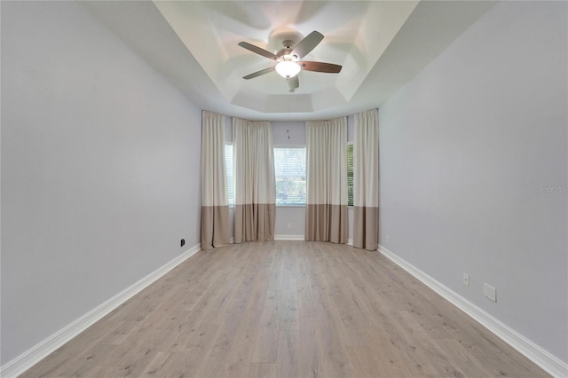 empty room with a tray ceiling, light hardwood / wood-style floors, and ceiling fan