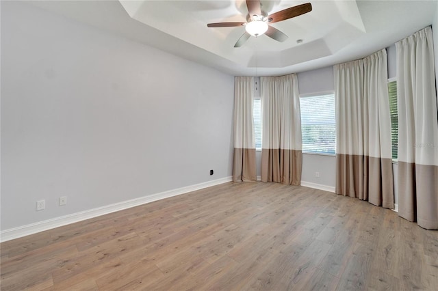 unfurnished room with a tray ceiling, ceiling fan, and light wood-type flooring