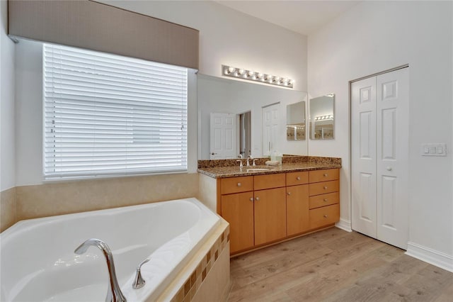 bathroom featuring hardwood / wood-style flooring, vanity, and a relaxing tiled tub