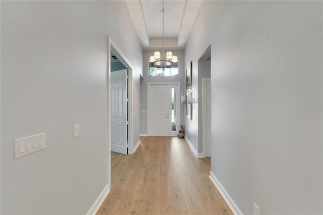 doorway to outside featuring an inviting chandelier, a towering ceiling, and light wood-type flooring