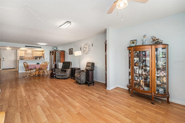 living area with ceiling fan, a textured ceiling, and light hardwood / wood-style flooring