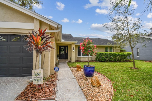 entrance to property with a garage, roof with shingles, a lawn, and stucco siding