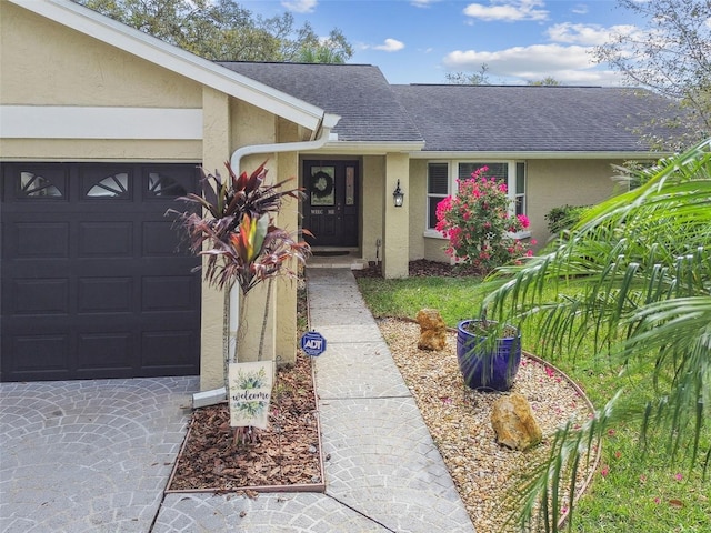 property entrance with an attached garage, roof with shingles, and stucco siding