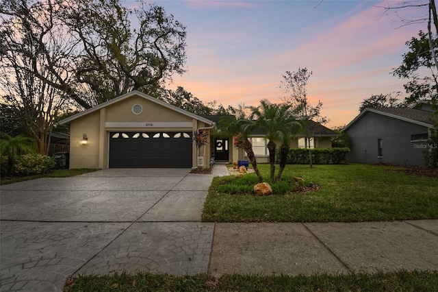 view of front of property featuring a garage, a yard, driveway, and stucco siding