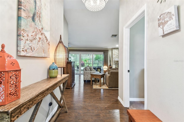 corridor with dark wood-type flooring, a chandelier, visible vents, and baseboards