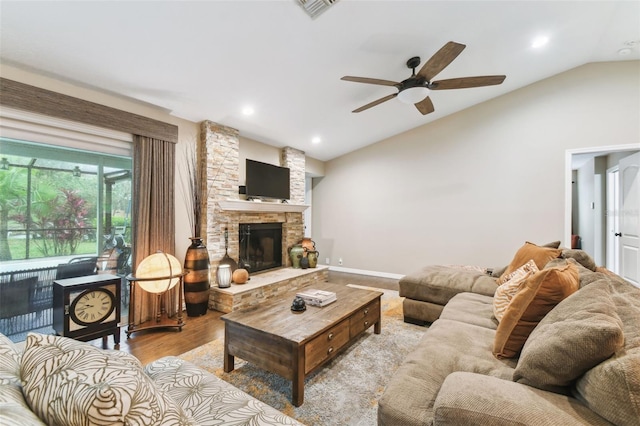 living room with lofted ceiling, visible vents, light wood-style flooring, a ceiling fan, and a stone fireplace