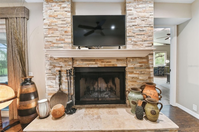 interior details featuring ceiling fan, a stone fireplace, wood finished floors, and baseboards