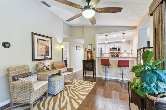 living area featuring lofted ceiling, ceiling fan, visible vents, baseboards, and dark wood finished floors