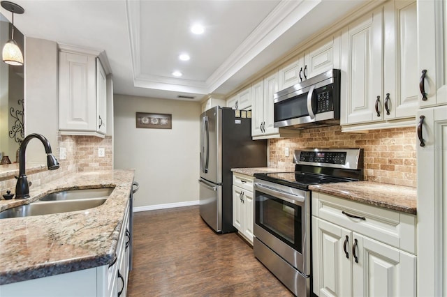 kitchen with a raised ceiling, stainless steel appliances, white cabinetry, pendant lighting, and a sink