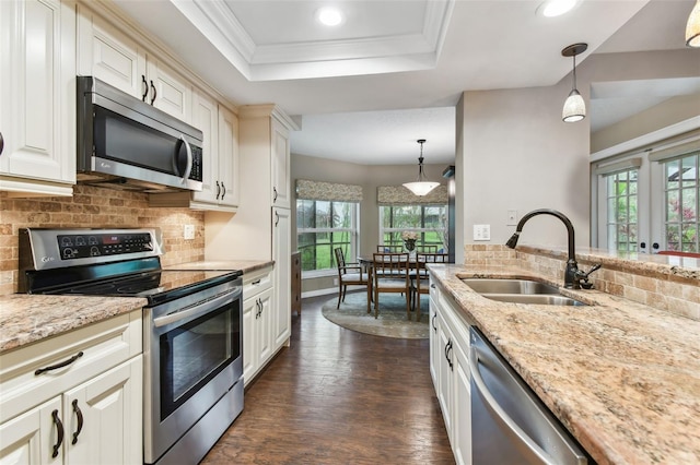 kitchen with light stone counters, decorative light fixtures, a raised ceiling, appliances with stainless steel finishes, and a sink