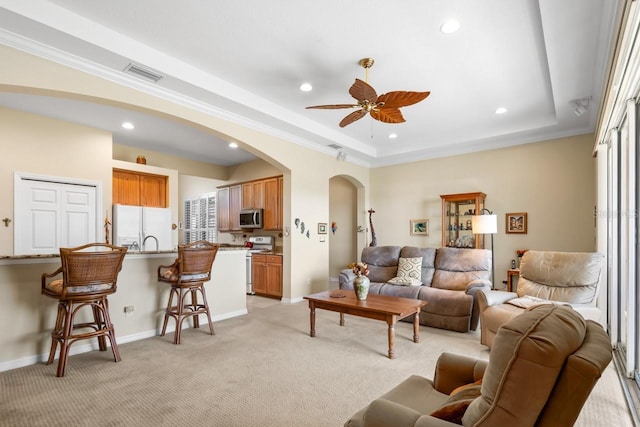 living room with light carpet, crown molding, a raised ceiling, and ceiling fan